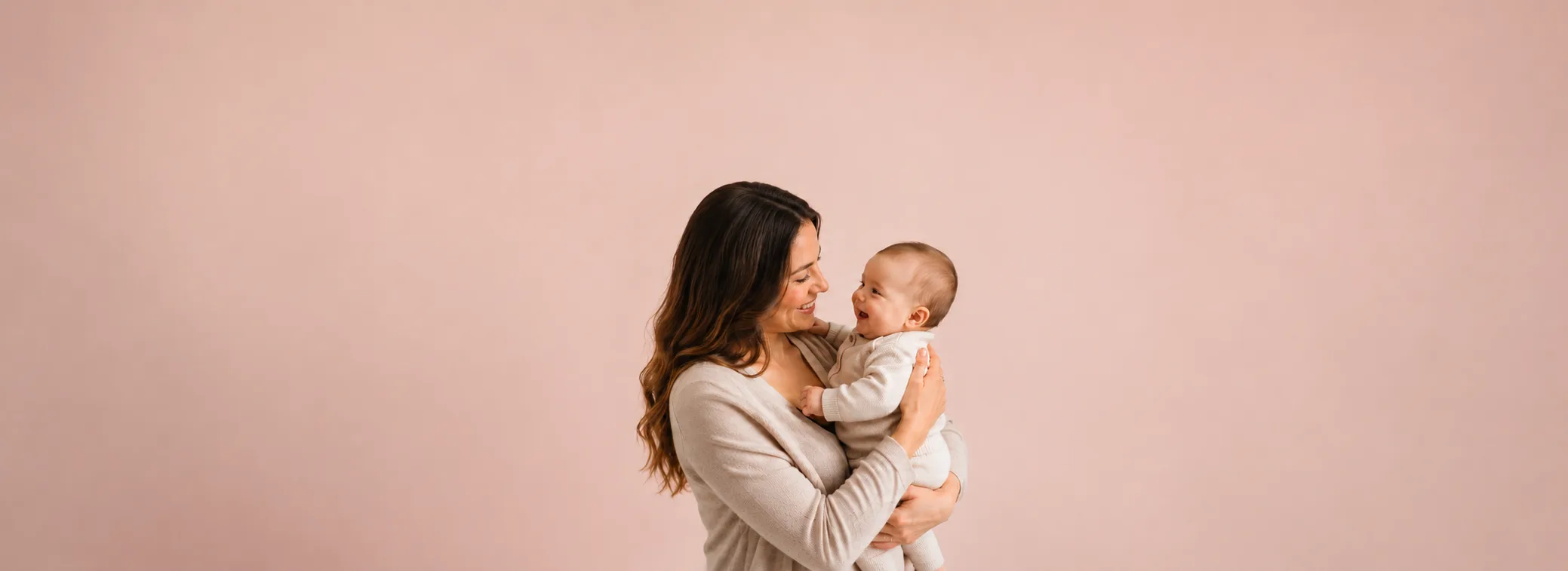 Mãe sorrindo com bebê no colo diante de parede rosa, banner da Mamii com cupons e promoções para mamães